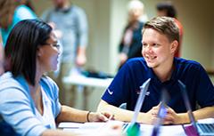 A male and female student working on laptops smiling